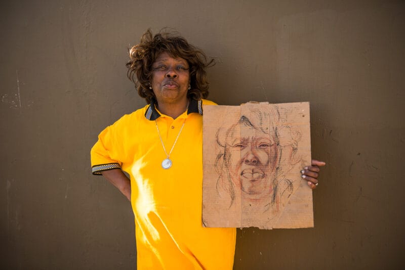 Roberta stand with her portrait drawn on cardboard on Skid Row
